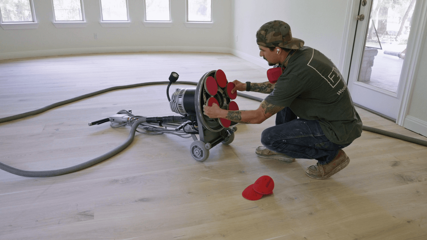 Hardwood flooring contractor changing sanding paper on a planetary flooring sander