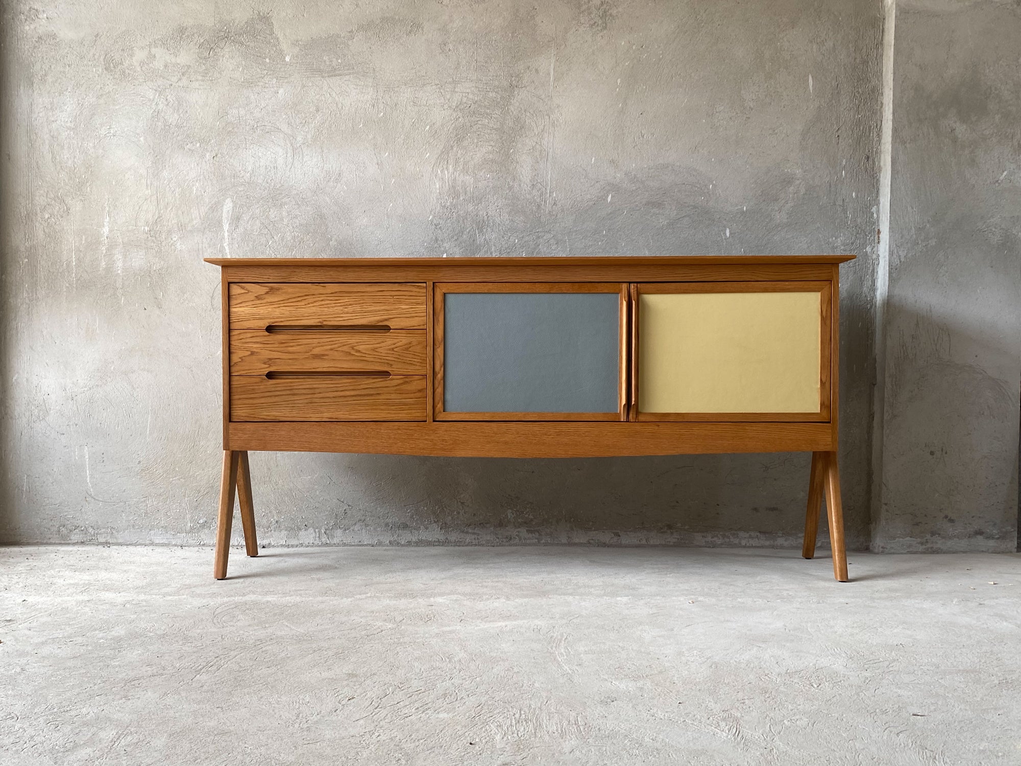 A mid-century modern sideboard crafted from white oak with three drawers and two cabinet doors finished with a hardwax oil wood finish.