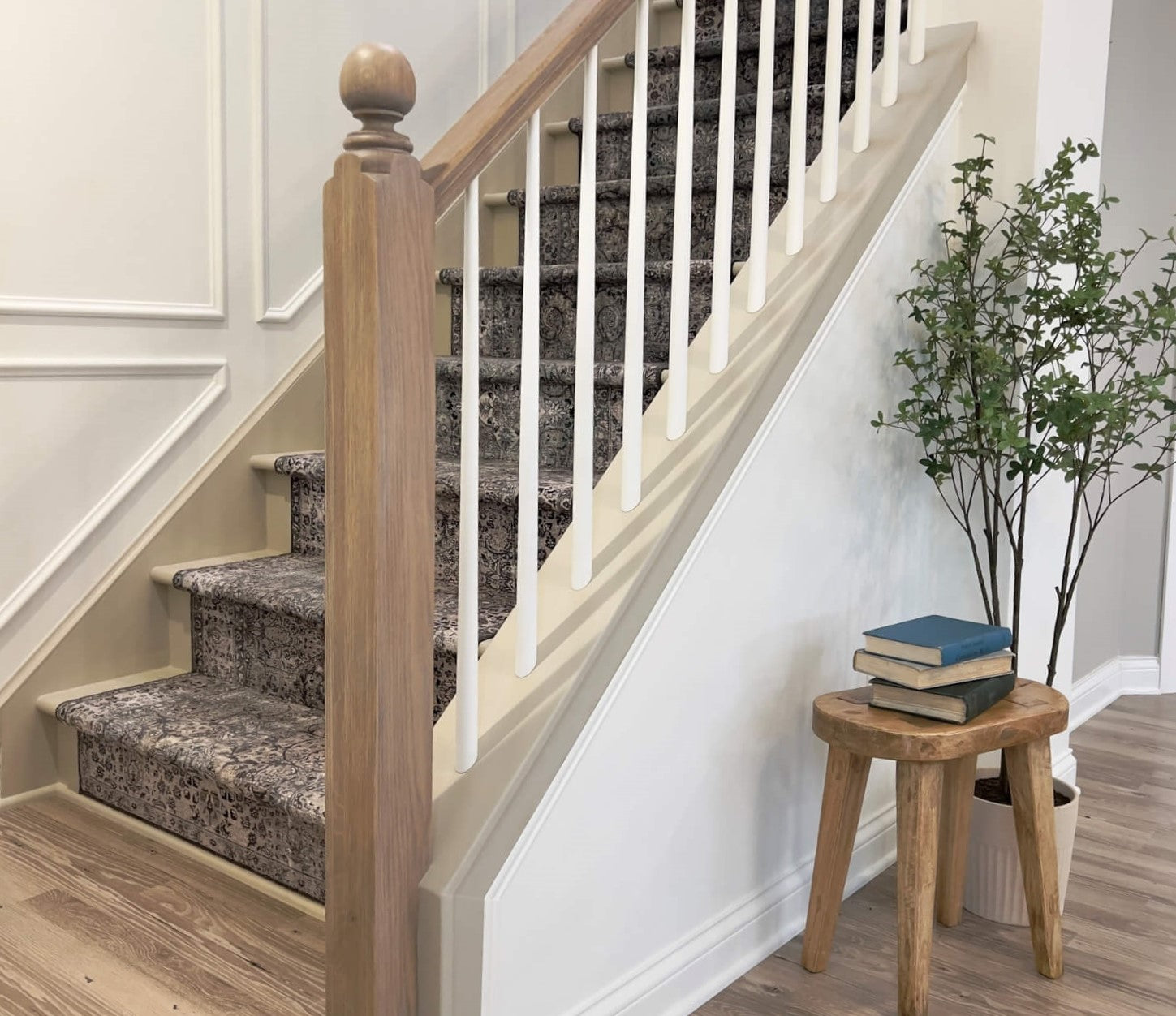 White oak stair railing complete with a stair post and rounded finial. Also pictured is a small vintage stool and potted tree.