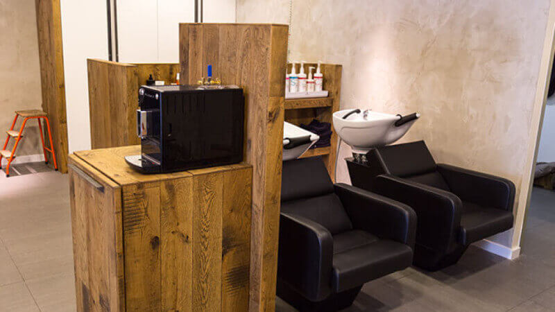 Two chairs in a barbershop with a wood cabinet standing beside it.