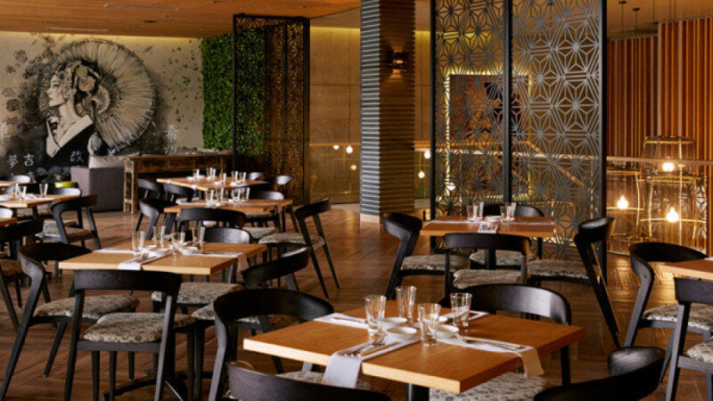 The beautiful interior of an asian restaurant with wood herringbone flooring and wood table tops.