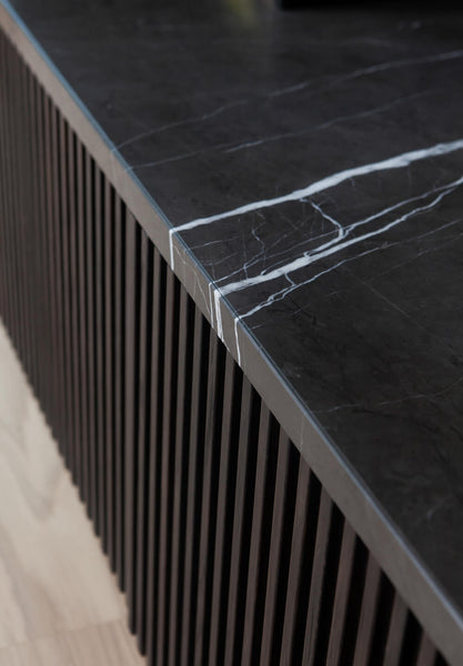 A close up of the slatted detail on a dark brown tv and book case. A marble slab is situated on top of the built-ins.