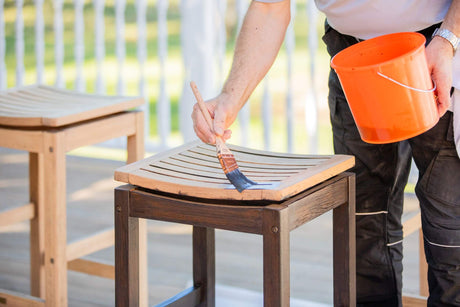 Man applying a dark wood stain color to a chair on a wood deck