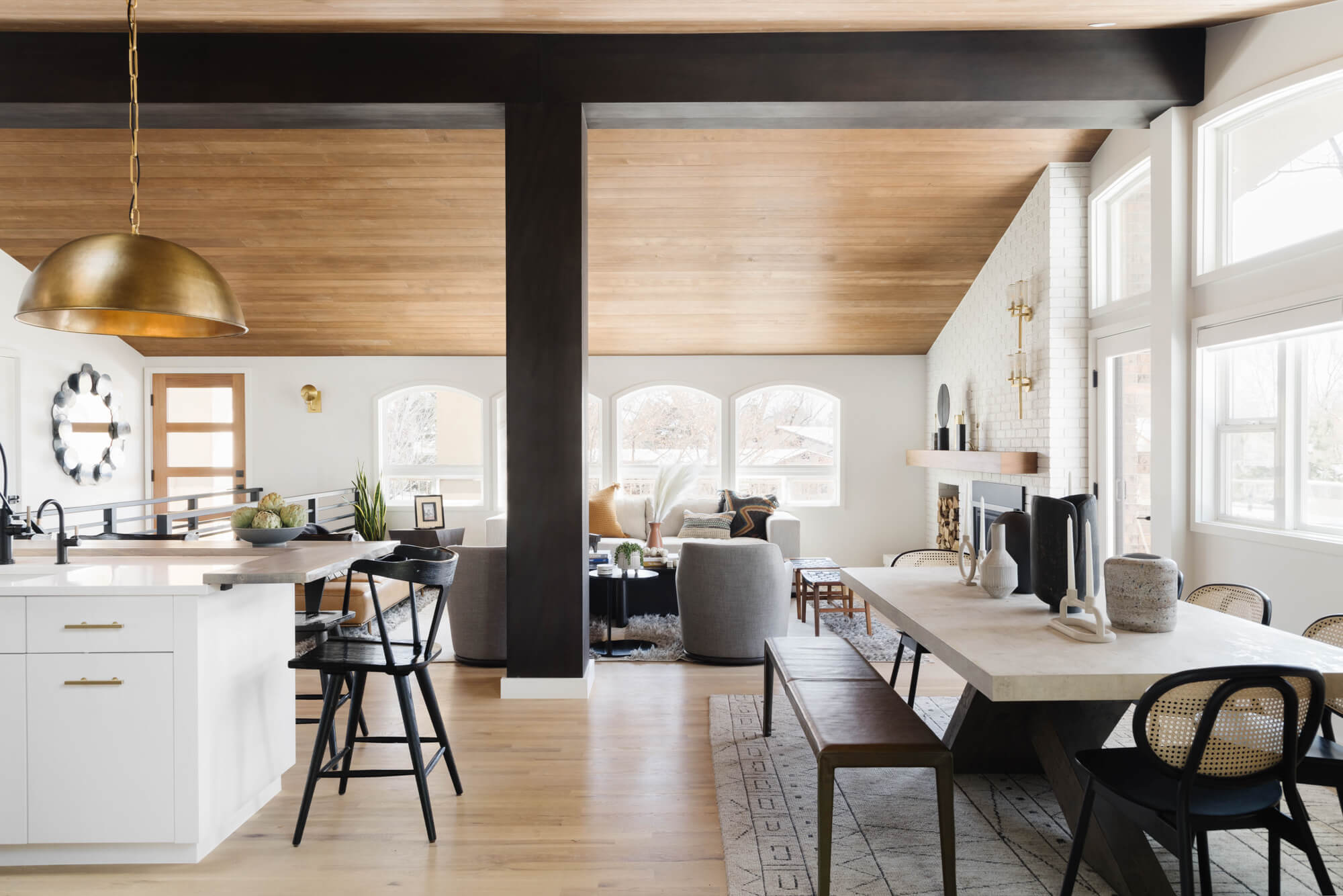 An updated 1970s home featuring wood flooring, a wood paneled ceiling, black beams and other mid-century modern inspired elements.