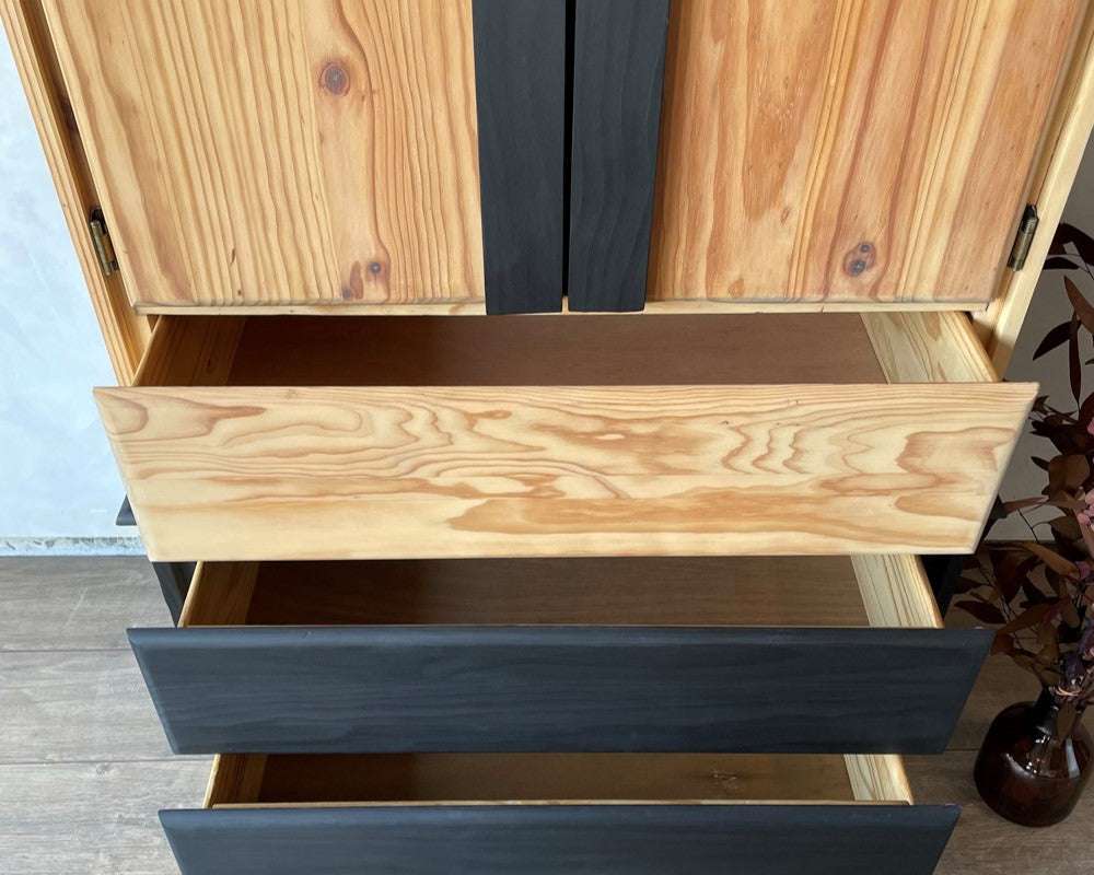 Two-toned pine armoire with it's drawers slightly ajar. 