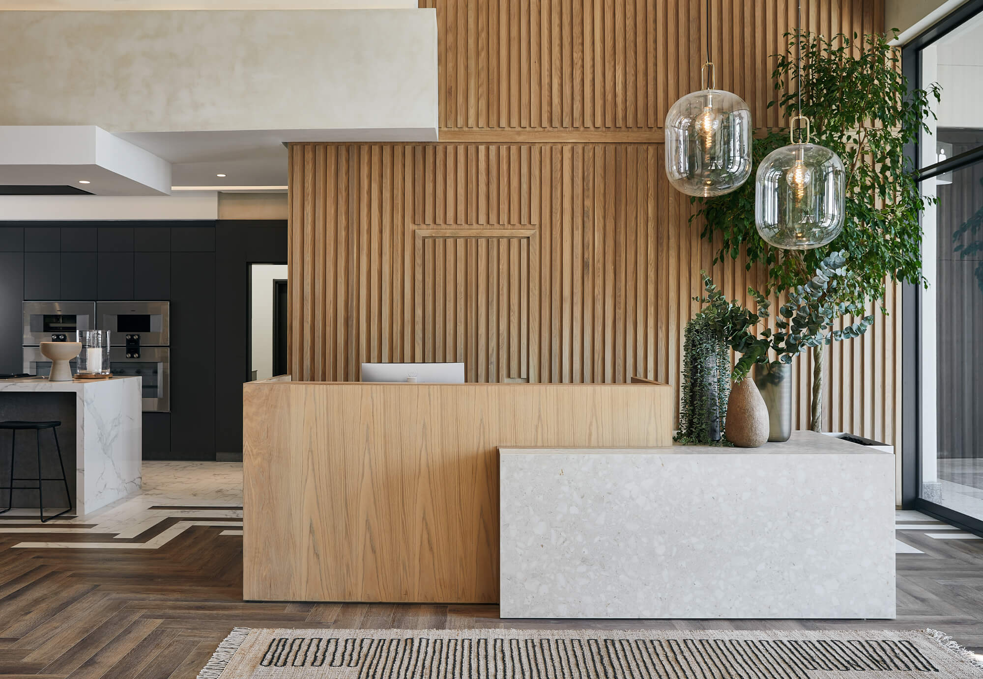 The entrance to a residential development office featuring a wood slatted wall and white oak reception desk finished with Oil Plus 2C in the color Mist.