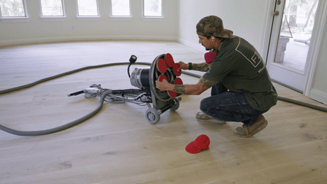 Hardwood flooring contractor changing sanding paper on a planetary flooring sander