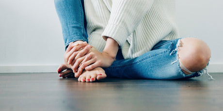 Barefoot woman in a sweater and blue jeans sitting on VOC free hardwood floor.