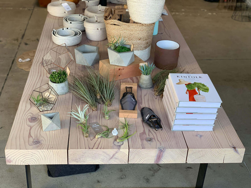 A thick redwood display table with a variety of retail items placed on it finished with Rubio Monocoat Oil Plus 2C hardwax oil.