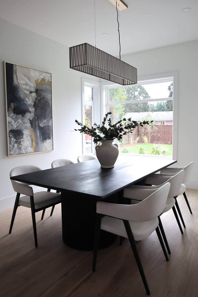 A large vase filled with greenery sits upon a white oak dining table surrounded by six chairs.