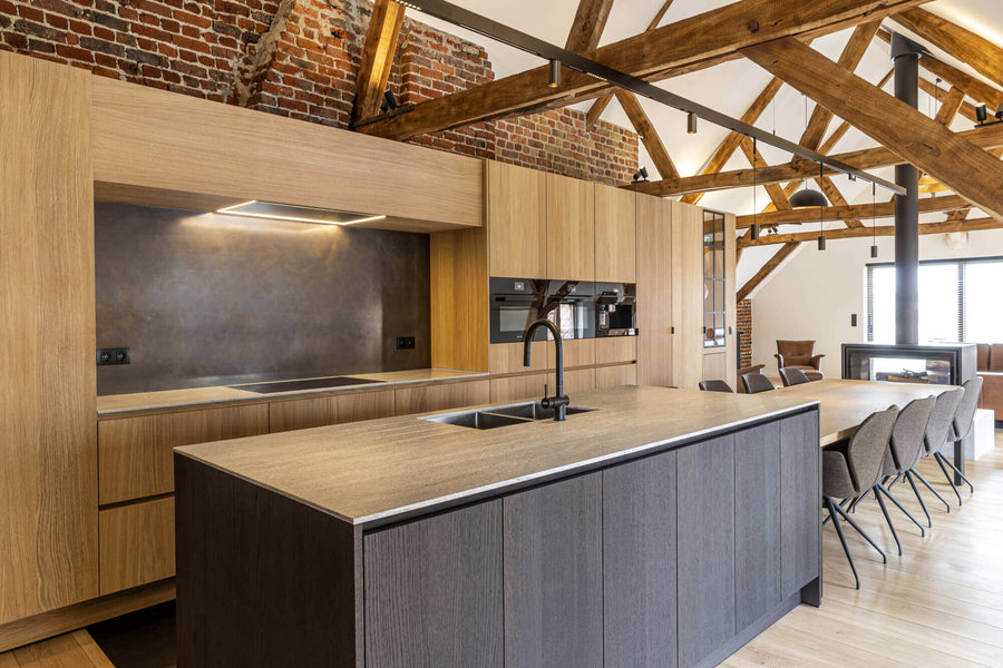 Kitchen with light wood cabinets and a dark brown island. Wood architectural beams and brick detail is seen throughout the attic kitchen.