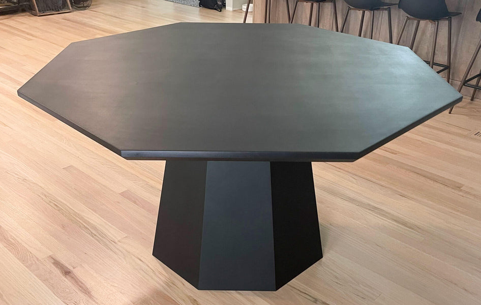 An image of a black maple dining table shaped like an octagon. The table's base is a tapered octagon shape.