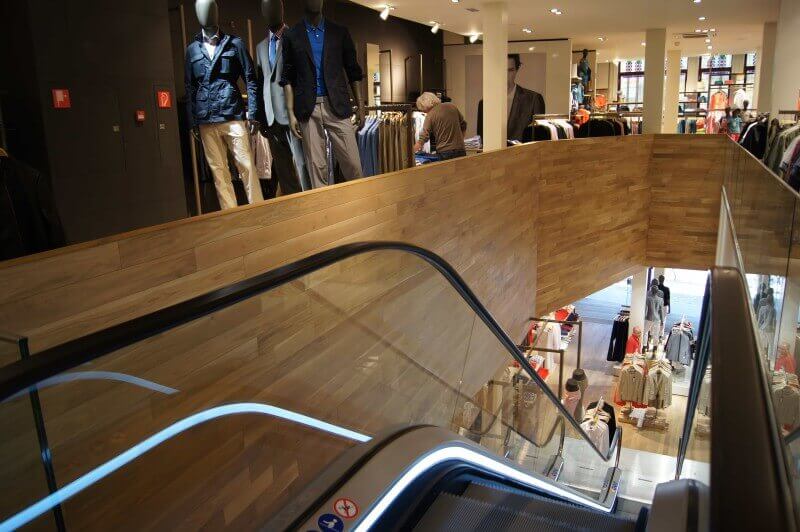 Escalator in clothing store with wood accent wall finished with hardwax oil.