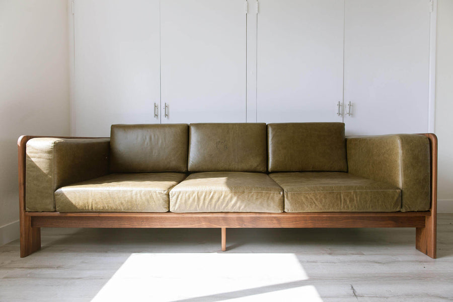 A custom sofa, with walnut wood base and olive green leather cushions.
