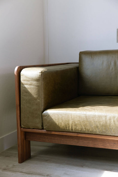 View of the arm of a custom walnut wood sofa with leather cushions.