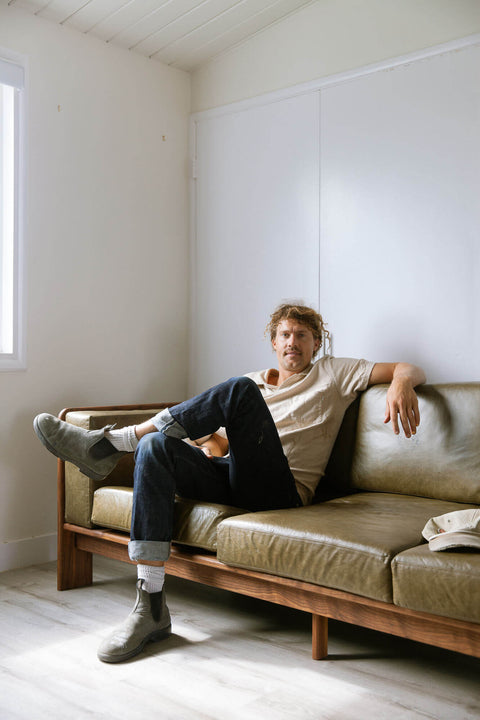 Man sitting on a custom handcrafted sofa with leather cushions and a walnut wood base.