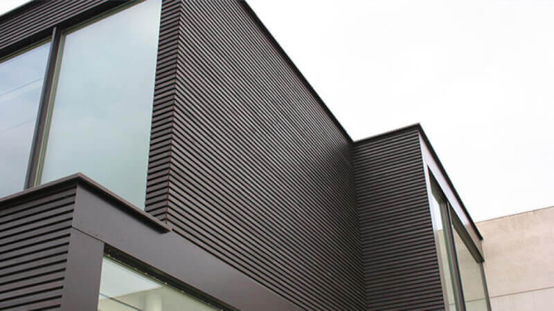 A close up of exterior wooden siding finished in a dark exterior wood oil.