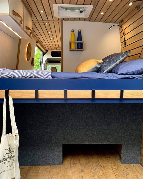 A camper vehicle bed with storage underneath. Oak accents can be seen on the ceiling finished with Rubio Monocoat Hybrid Wood Protector.