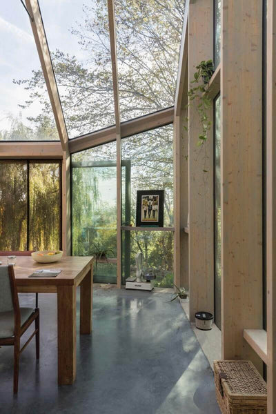 Wood beam and glass sun room with table inside.