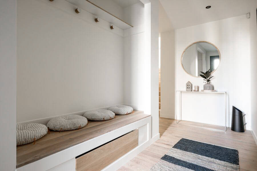 Mudroom with white walls and natural hardwood flooring and bench.
