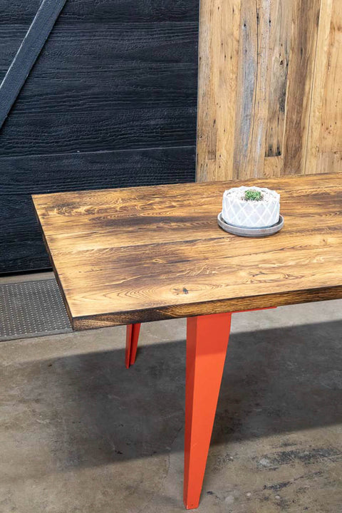 A charred white oak dining table with orange metal legs finished with Rubio Monocoat Oil Plus 2C "Pure".