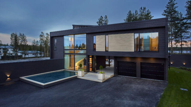 Architecturally modern wood house with straight lines and a driveway with a pool beside it.