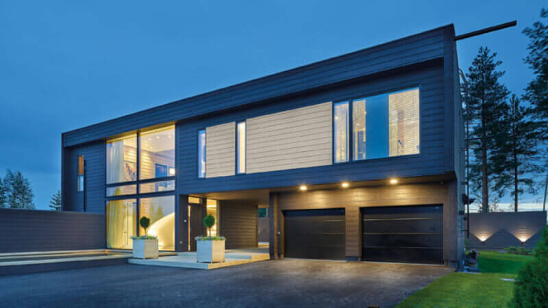 The front of a modern home with big windows and wood siding at dusk.