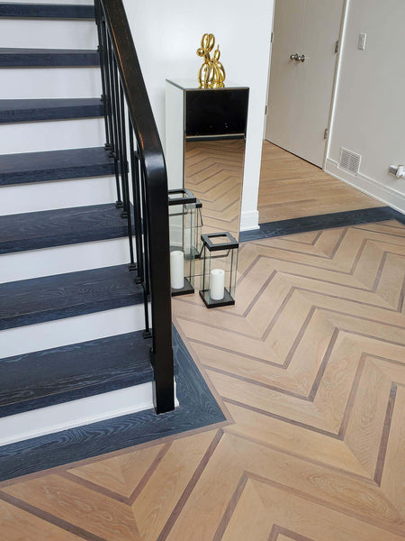 Wood stairs with a cerused finish and chevron hardwood flooring pattern in an entry foyer.