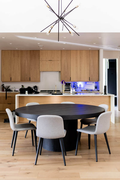 A view with around dining table in the foreground and a kitchen in the background.