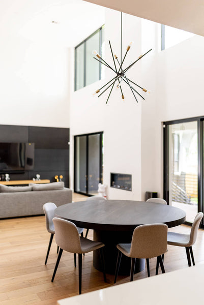 A modern round dining table sits in the foreground with a contemporary light fixture hanging above it.
