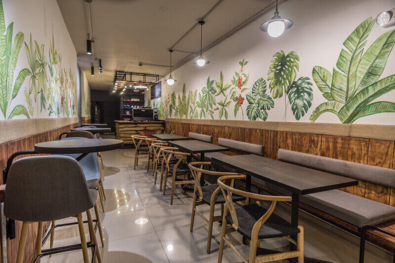 The inside of a long narrow earthy coffee shop, with seating running down both sides of the room.
