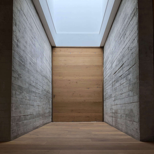 A concrete hallway with white oak flooring and door at the end.