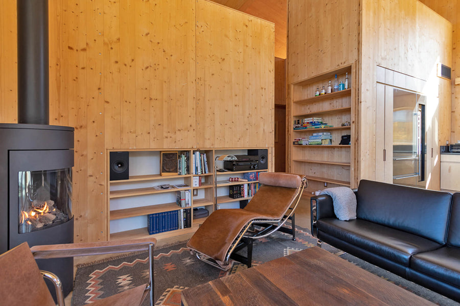 A modern lodge living room with a wood burning fireplace stove. leather lounge chair and sofa, and shelving built in to the wood details.