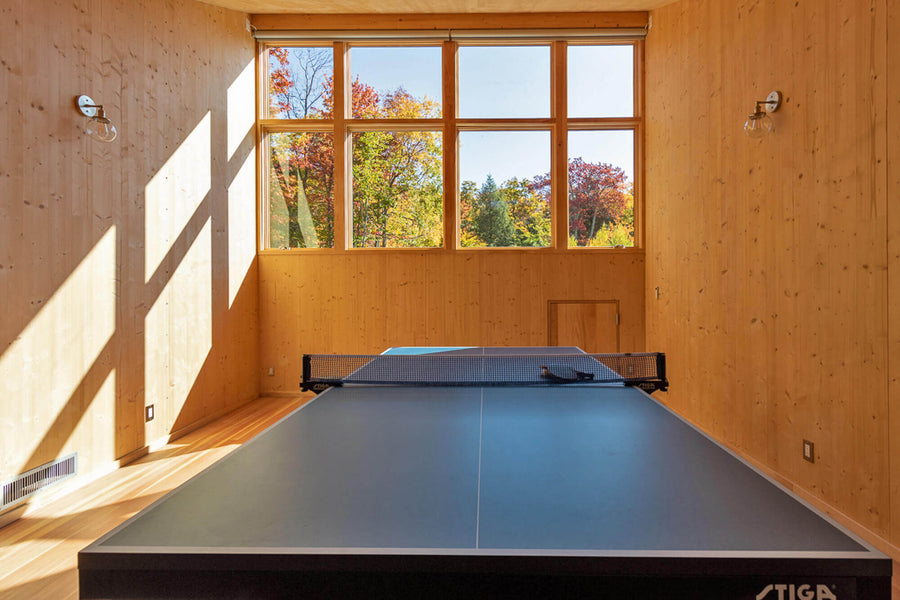A game room featuring a ping pong table with large windows looking out to the tree filled landscape.