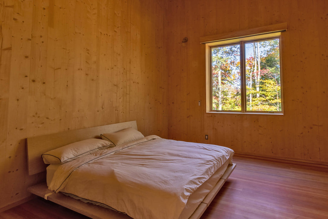 A secondary bedroom with wood flooring and wood paneled walls finished with Rubio Monocoat Oil Plus 2C.
