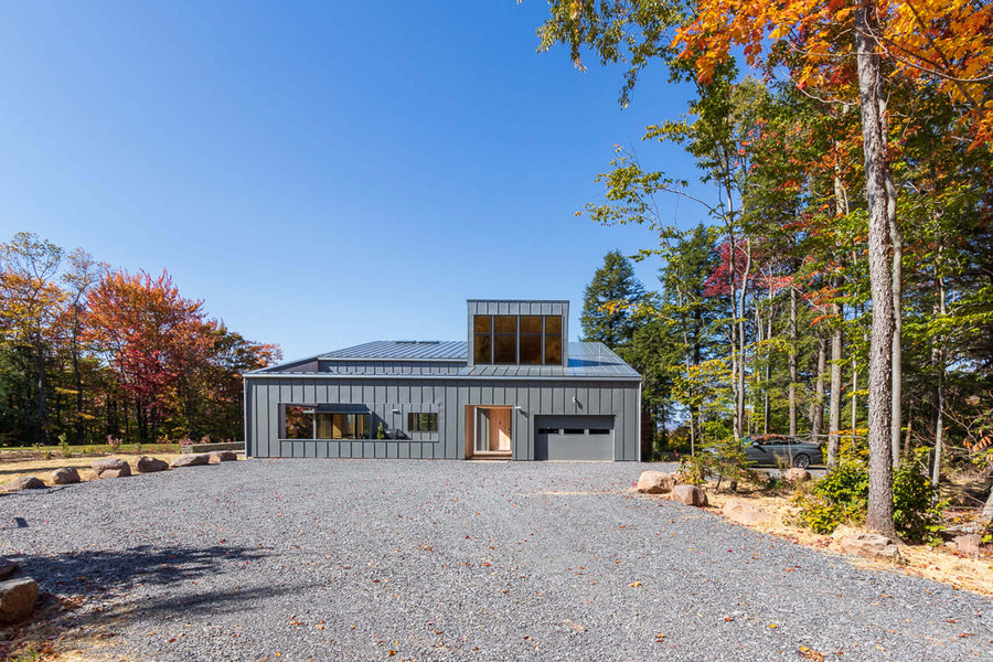 The backside of the Berghaus Hunter contemporary lodge home. Windows, a garage door and a path leading to the front entrance is pictured.