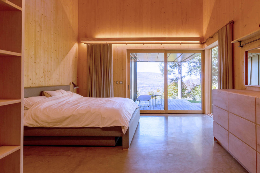 A modern bedroom with wooden walls and ceilings. Birch six-drawer dresser finished with Rubio Monocoat Oil Plus 2C. The bedroom also features two glass doors leading out to a wooden deck.