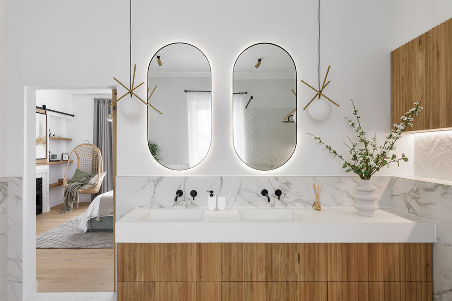 Bathroom with a white oak slatted vanity with two oval mirrors and modern light fixtures.