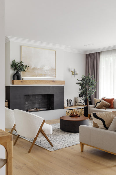 Living room with light wood flooring, modern accent chair, fireplace surrounded by black stone with a white oak wood beam.