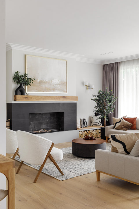 Living room with light wood flooring, modern accent chair, fireplace surrounded by black stone with a white oak wood beam.