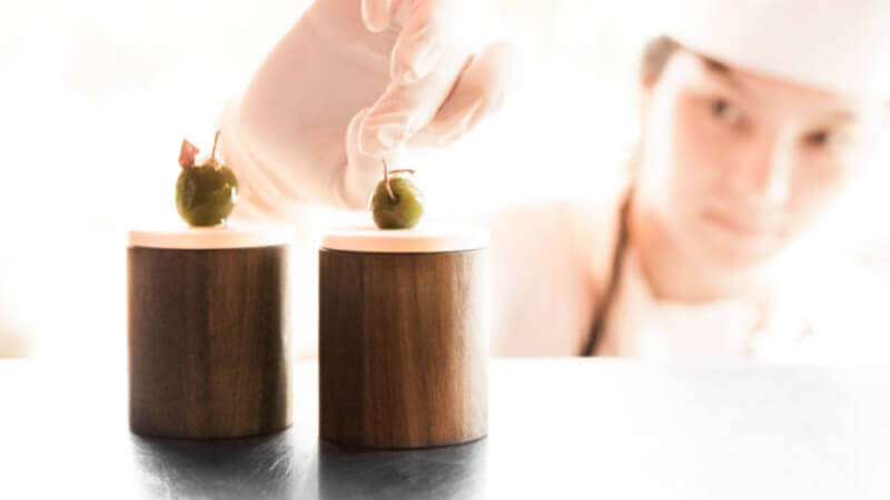 A chef placing olives on top of 2 round wooden serving utensils.