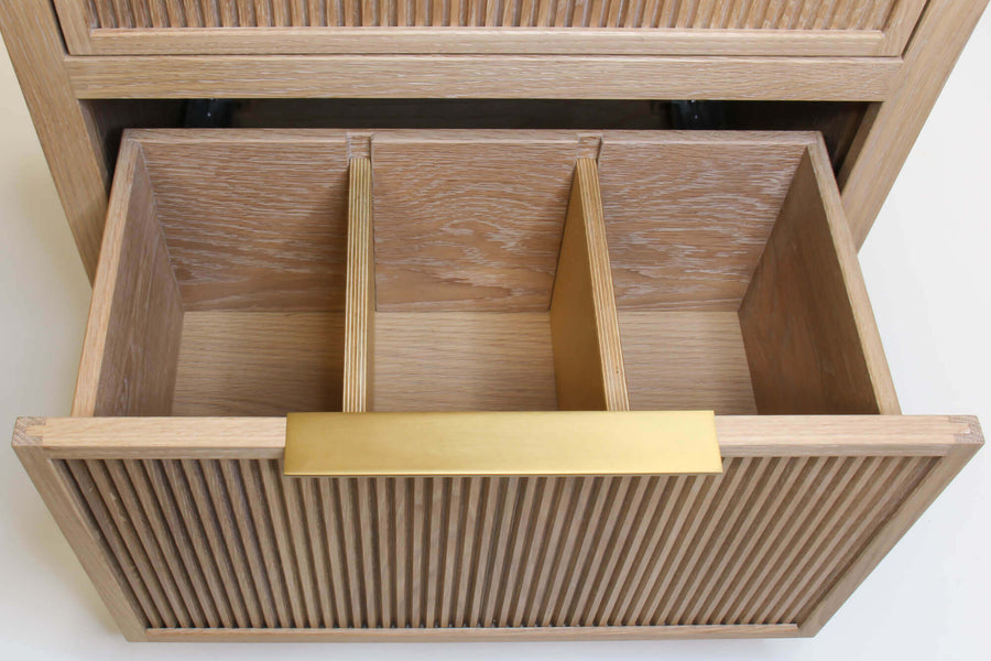 An open white oak storage dresser drawer complete with dividers and a brass drawer pull.