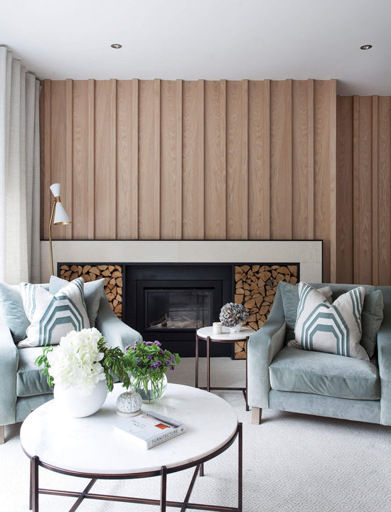 White oak slat wall in Rubio Monocoat Oil Plus 2C Natural spans a living room fireplace, with vertical fluting drawing the eye up from the stone hearth.