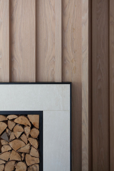 Macro detail where white oak fluted paneling in Rubio Monocoat Oil Plus 2C Natural meets a stone and blackened-wood fireplace frame.