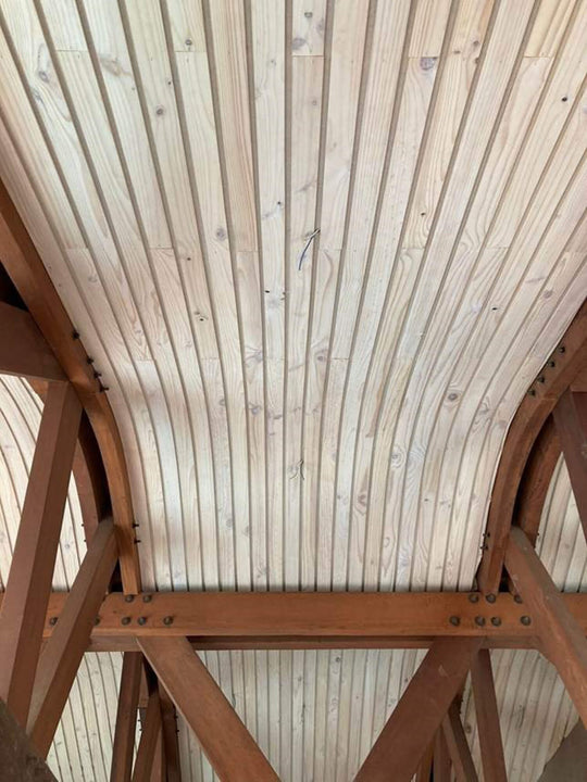 Detail of exposed timber roof trusses and beam joinery finished in Rubio Monocoat, with globe pendant lights hanging beneath the curved wood-slat ceiling.