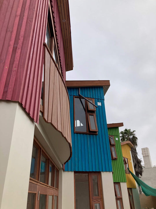 Upward view of Aynimundo's multicolored wood-clad towers in pink, blue, green, and yellow, each finished in Rubio Monocoat and fitted with wood-framed windows.