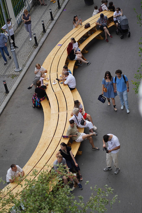 Multiple people sitting at a large, winding picnic table crafted from spruce and finished with Rubio Monocoat DuroGrit "Grassland Beige".