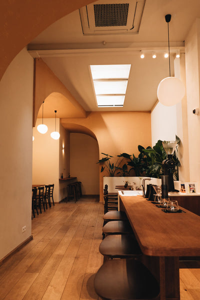 A seating area in a coffee bar featuring a long table and chairs and several spherical light fixtures.