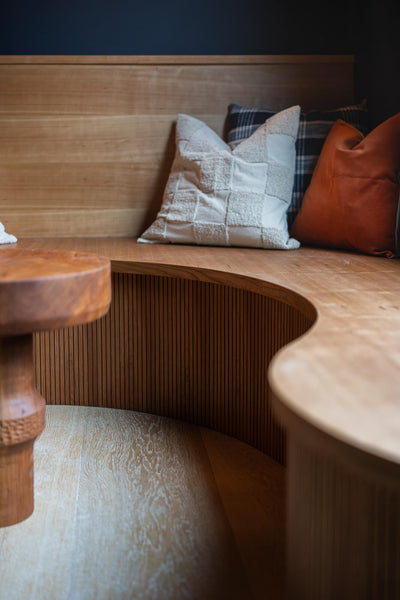 Cherry seating area with a curved detail. This space also features a small round table and several throw pillows. 