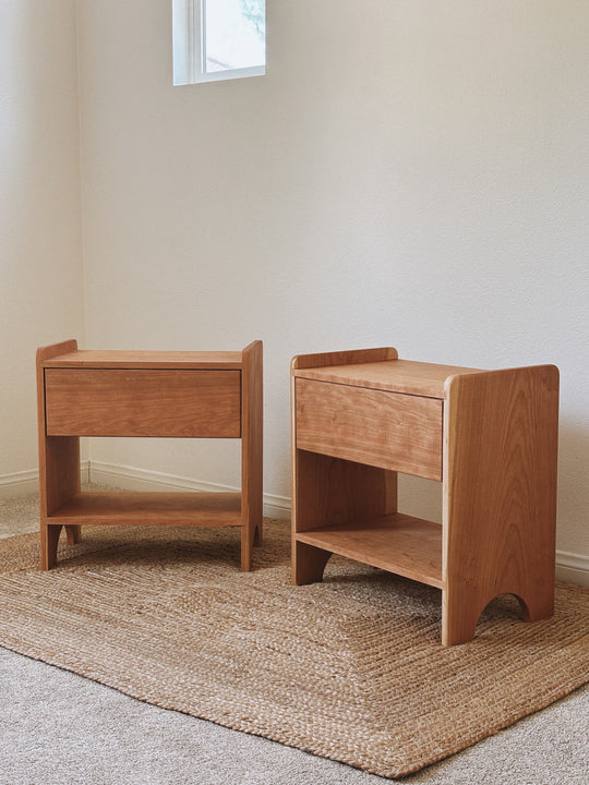 Solid cherry wood nightstand with one drawer and open lower shelf, finished with Rubio Monocoat Oil Plus 2C Pure, angled side view on jute rug